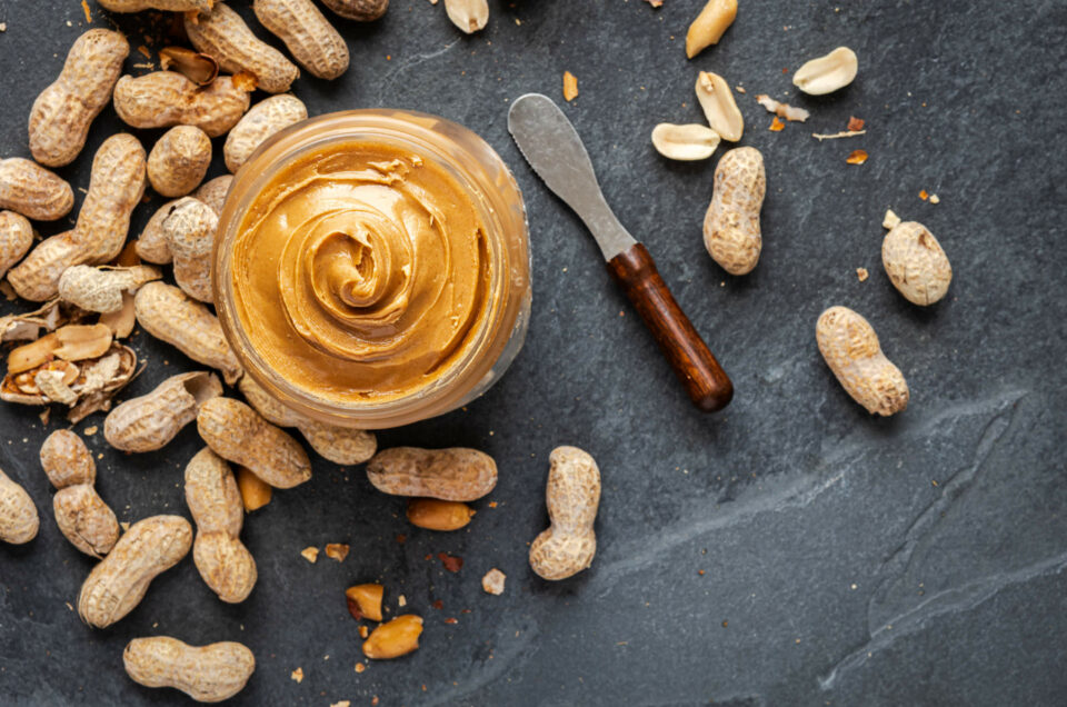 An overhead view of a jar of peanut butter surrounded by un-shelled peanuts.